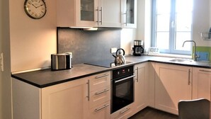 Een moderne keuken met witte kastjes, een inbouwoven, een waterkoker en een koffiezetapparaat.