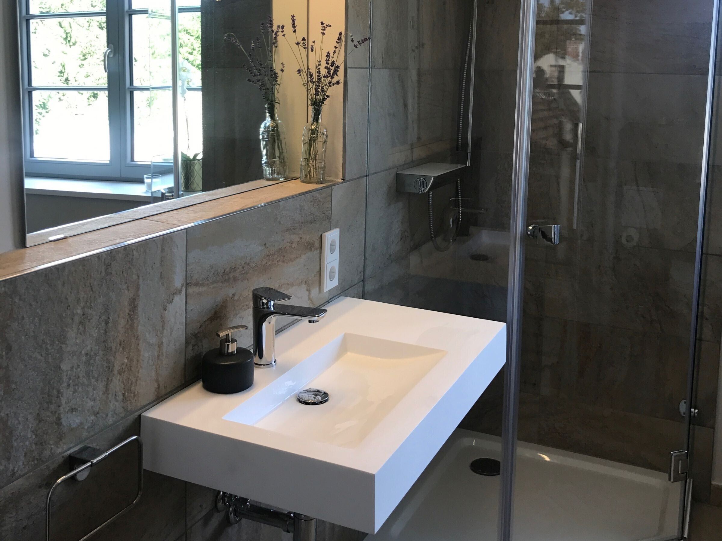 Ein modernes Badezimmer mit einem weißen Waschbecken, einer Duschkabine aus Glas und einem Spiegel über dem Waschbecken.