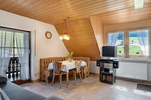 Una habitación acogedora con techo de madera, una mesa de comedor con sillas, un sofá, un televisor y una estantería.
