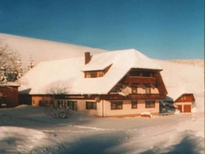 Un chalet cubierto de nieve con techo inclinado, una chimenea y un pequeño porche.
