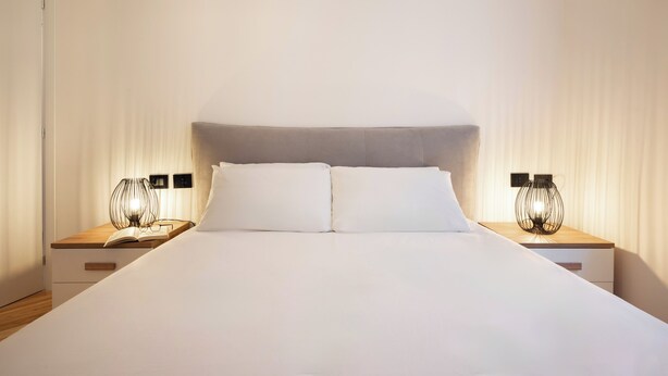 A neatly made bed with white linens, two bedside tables with lamps, and a wooden headboard.