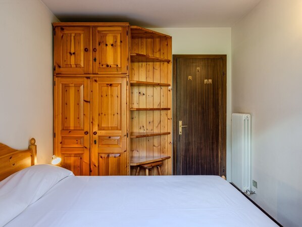 A bedroom with a wooden wardrobe, a bed, a radiator, and a door.