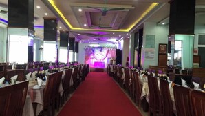 A banquet hall with rows of tables and chairs, a red carpet, and a stage with a purple backdrop. - Minh Hanh Hotel Sam Son -BAY LUXURY (Sam Son)