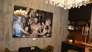 Comedor con una amplia fotografía en blanco y negro en la pared, una araña y un aparador de madera con un reloj.