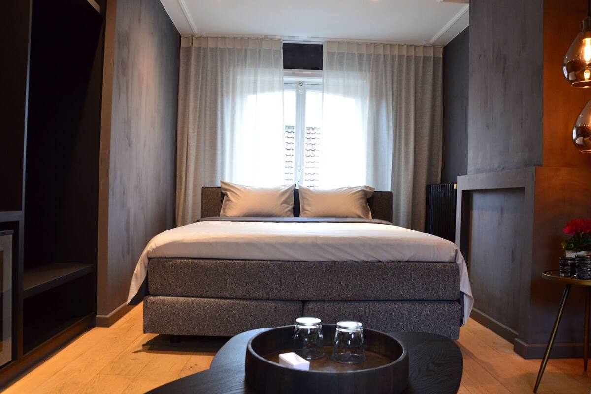 Un dormitorio moderno con una cama grande, una mesita de noche con dos vasos y una ventana con cortinas.