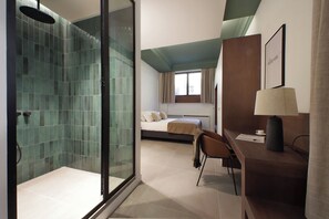 A hotel room with a glass shower enclosure, a bed with a view, a desk with a lamp, and a chair. - Crispi Loft (Rome)