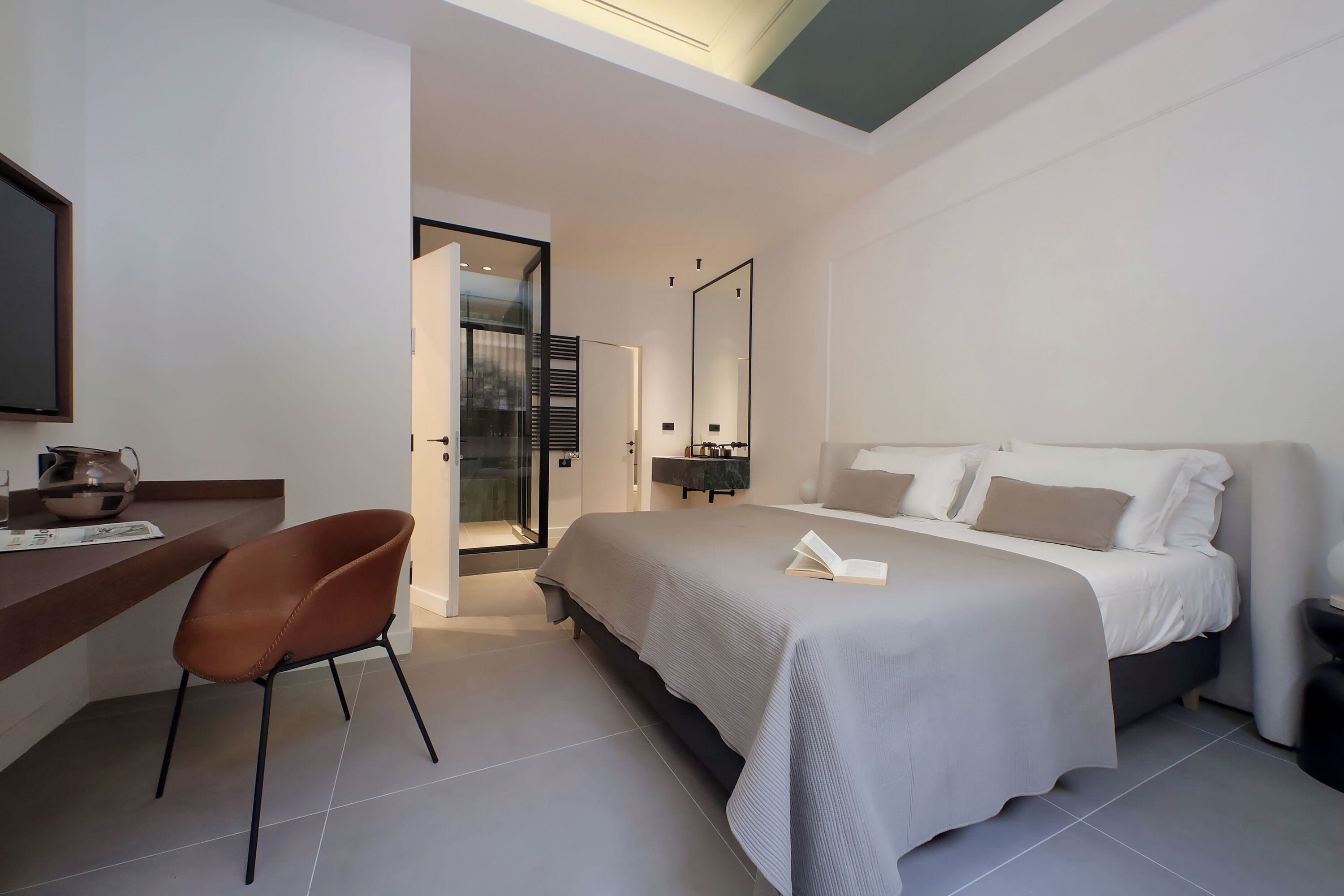 Una habitación de hotel moderna con una cama grande, un escritorio con una silla, un espejo y vistas a la ciudad por la ventana.