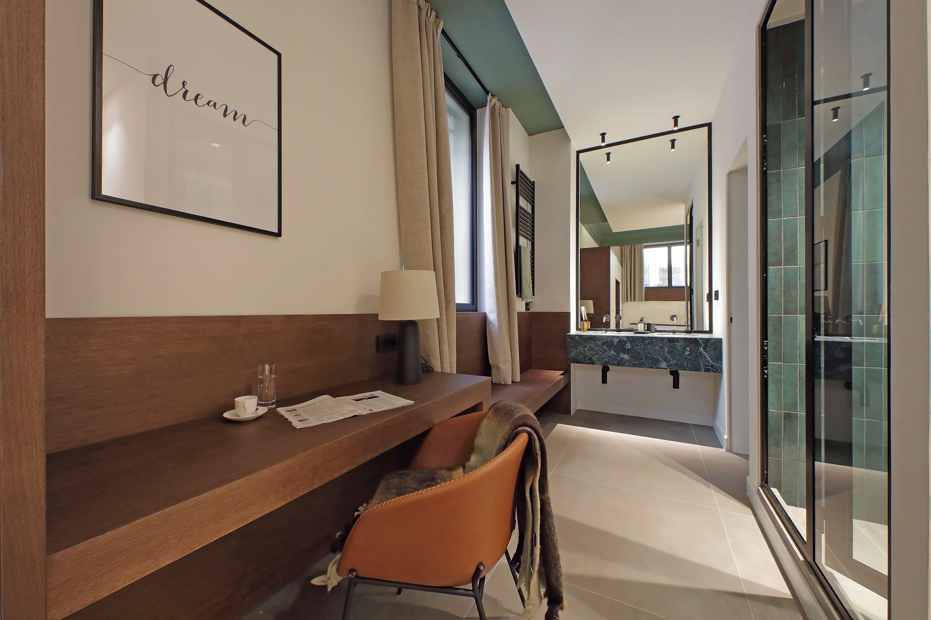 Una camera d'albergo moderna con una scrivania in legno, una sedia, uno specchio e un'ampia finestra.