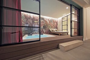 A modern indoor pool area with a tropical mural, wooden deck, and a lounge chair. - Crispi Loft (Rome)
