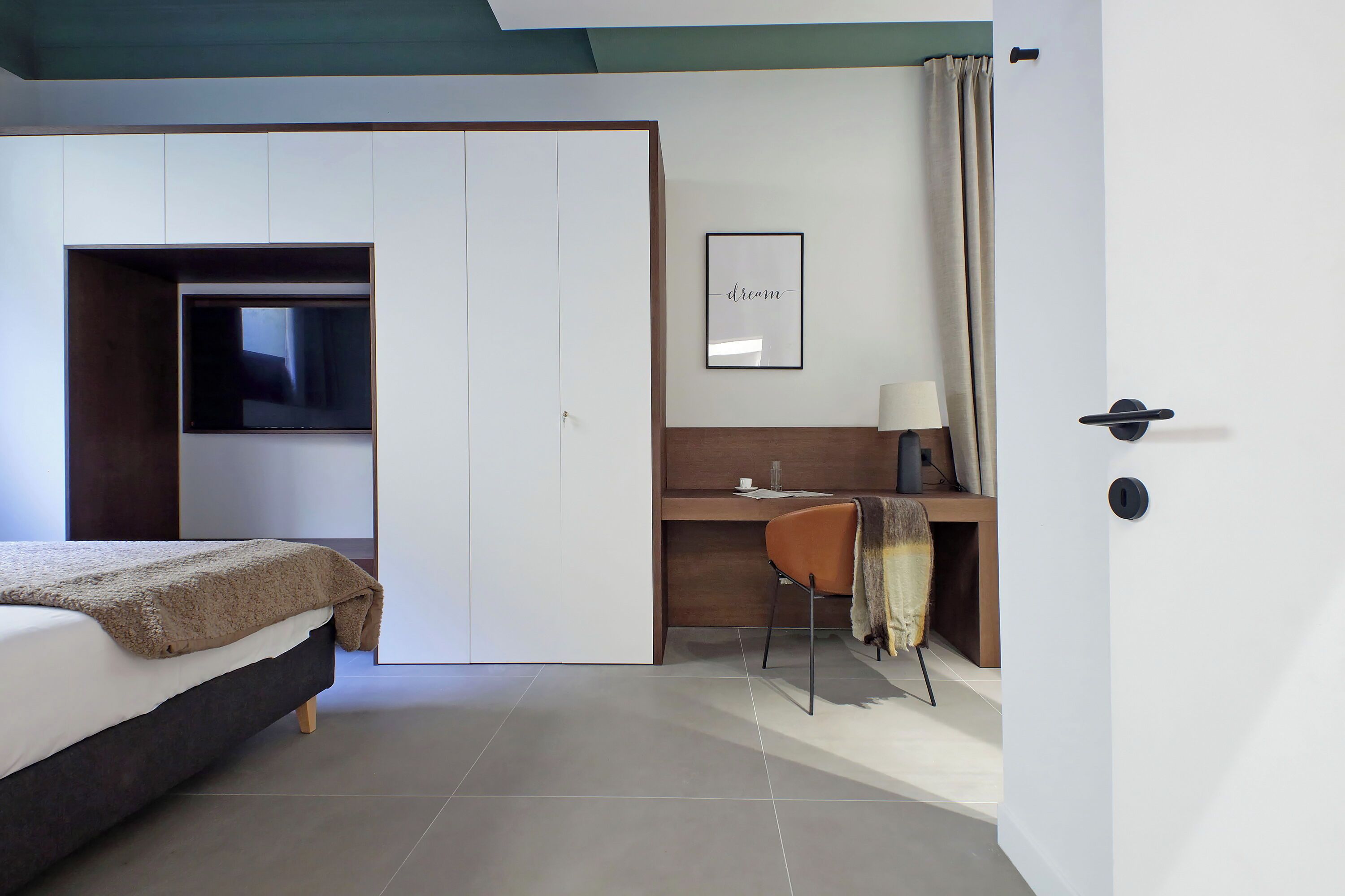 A bedroom with a bed, a desk, a chair, a wardrobe, and a framed picture on the wall.