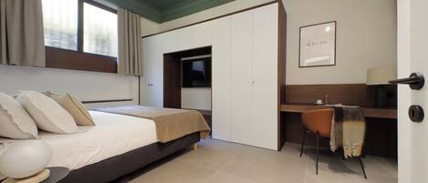 A modern bedroom with a bed, a desk, and a chair. There is a window with curtains, a framed picture on the wall, and a door.