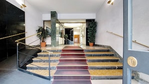 Un escalier avec des marches en marbre et une moquette rouge menant à une porte dotée d’une poignée en laiton.