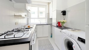 Une cuisine moderne avec des meubles blancs, une cuisinière à gaz, un four encastré, un évier et un lave-linge.