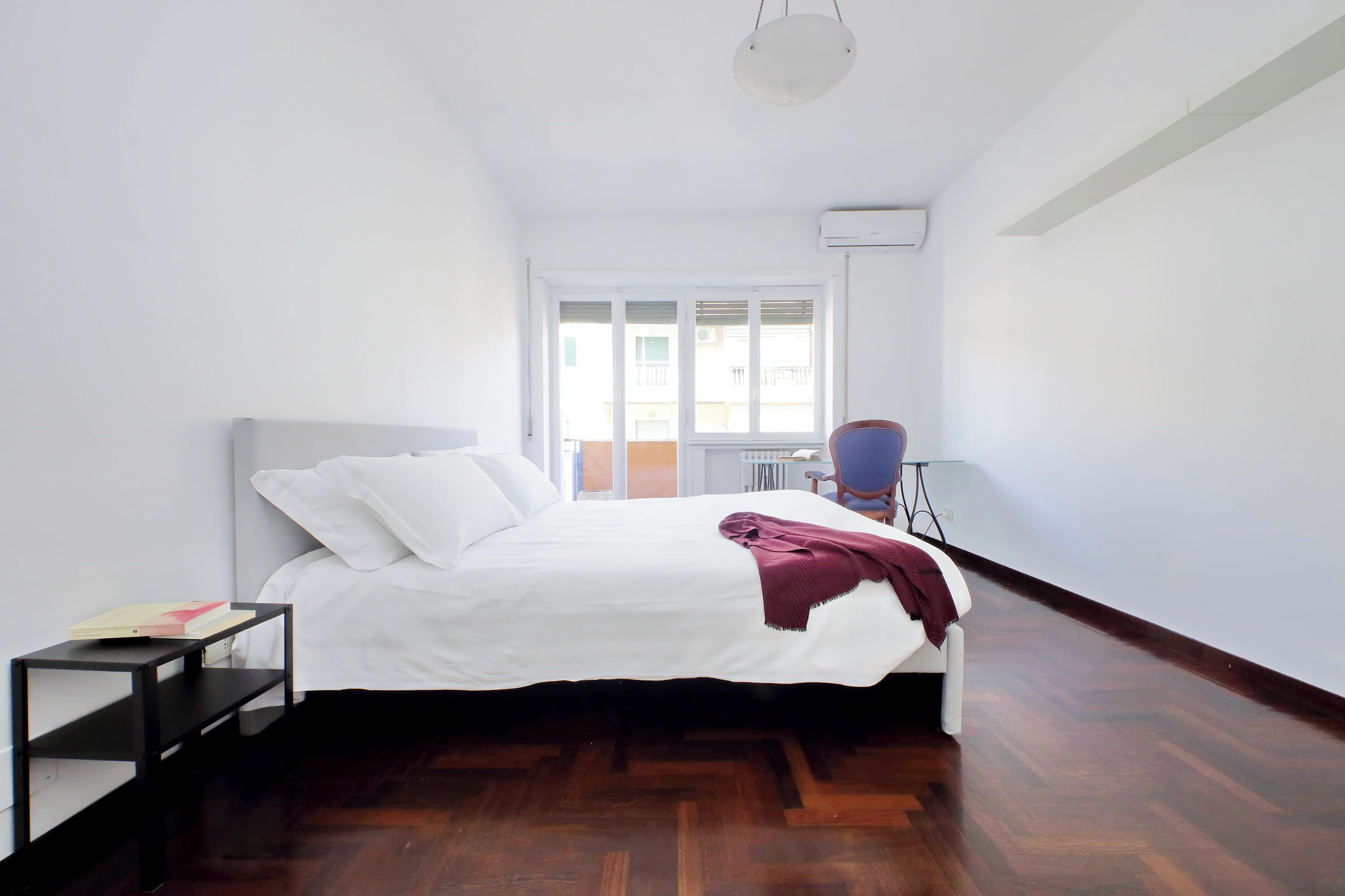 A bedroom with a bed, a nightstand, a chair, a window, and a radiator.