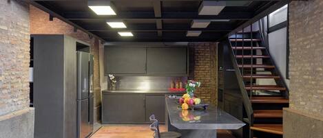 Een kleine keuken met een centraal eiland, een koelkast en een trap naar een hoger niveau.