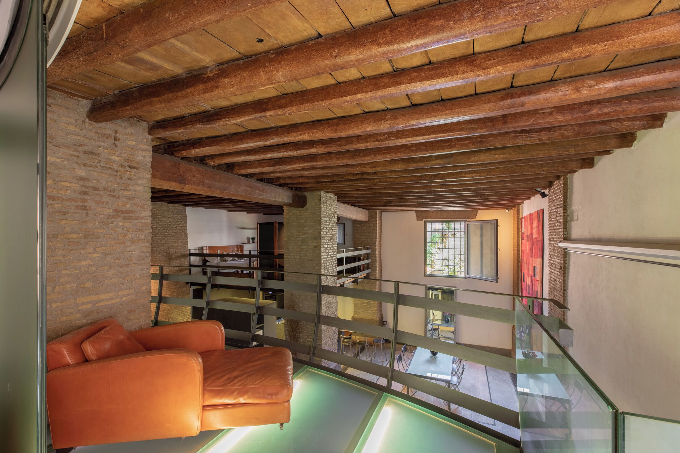 A spacious loft with exposed wooden beams, a leather sofa, and a glass railing overlooking a lower level.