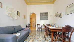 A living room with a sofa, dining table, chairs, and a patterned floor. - Cozy Merulana (Rome)