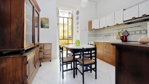 A kitchen with wooden cabinets, a dining table with chairs, and a window with stained glass. - Cozy Merulana (Rome)