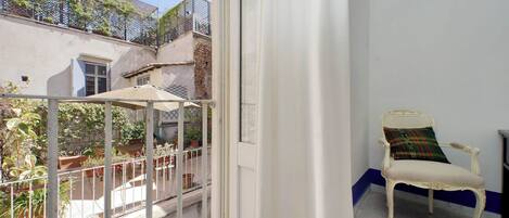 A balcony with a white chair and a small table, surrounded by potted plants and a metal fence.