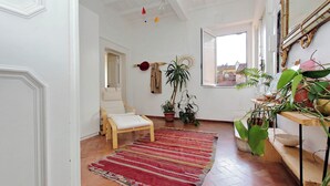 A room with a wooden chair, a red and beige striped rug, potted plants, and a large mirror on the wall. - Charming Minerva (Rome)