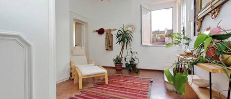 A room with a wooden chair, a red and beige striped rug, potted plants, and a large mirror on the wall.