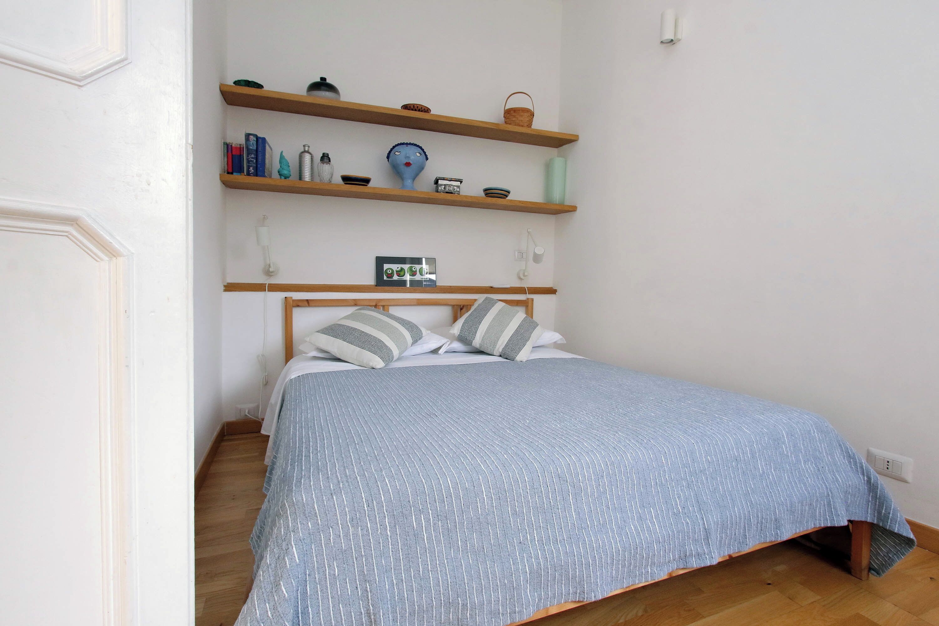 A bedroom with a bed, wooden shelves above, and a bedside table.