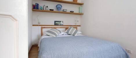 A bedroom with a bed, wooden shelves above, and a bedside table.
