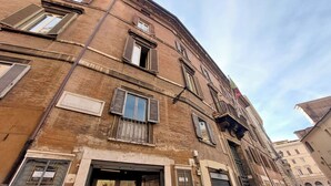 A multi-story building with a brown facade, multiple windows with shutters, and a ground-level entrance with a glass door. - Charming Minerva (Rome)