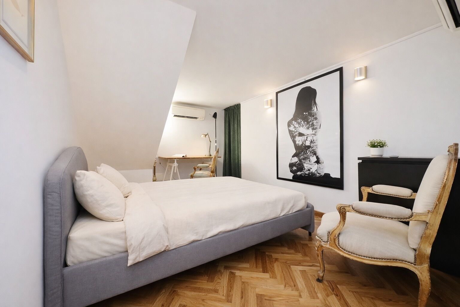 Ein Schlafzimmer mit Bett, Sessel, Schreibtisch und Wandlampe.