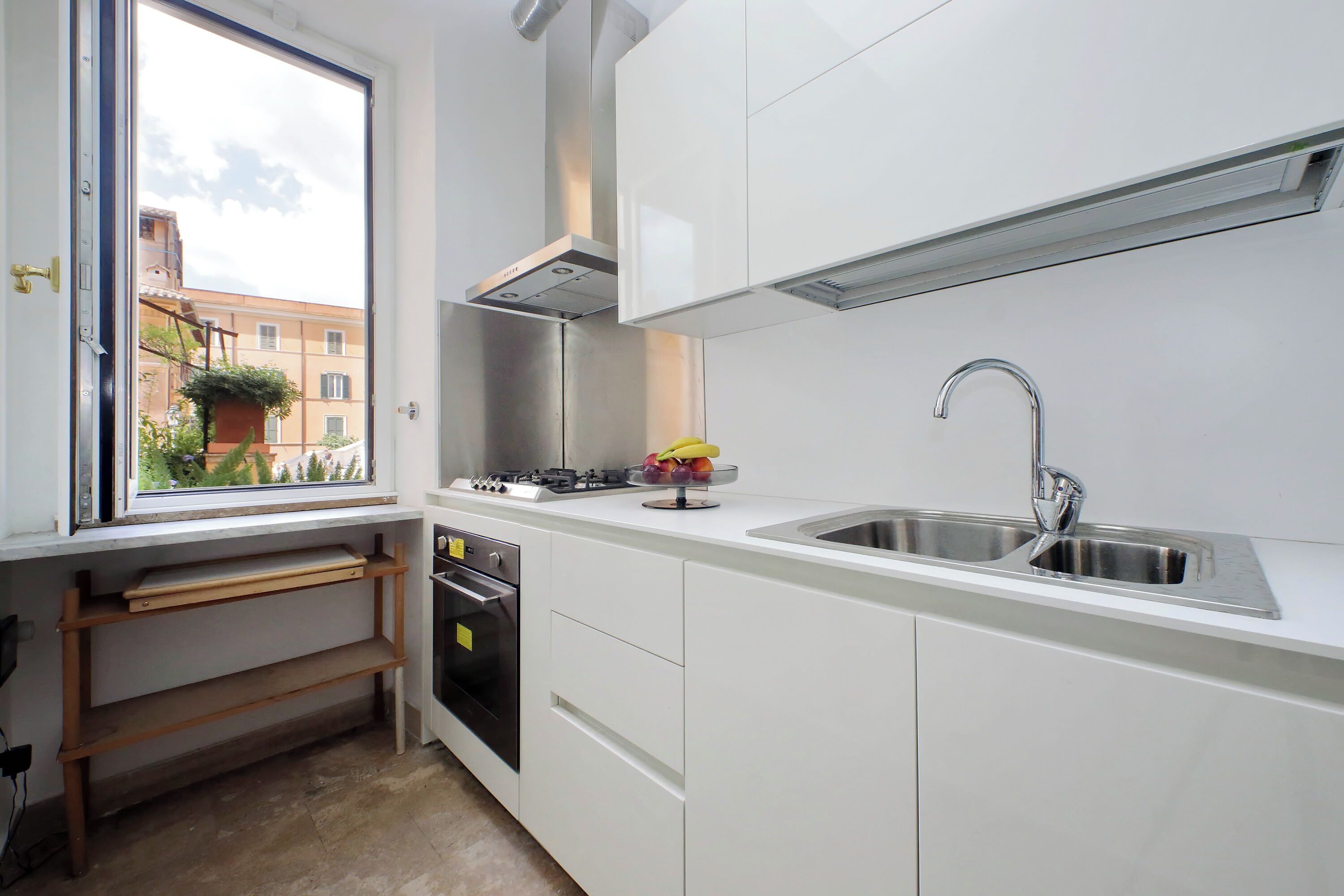 A modern kitchen with white cabinets, a stainless steel sink, and a window overlooking a building.