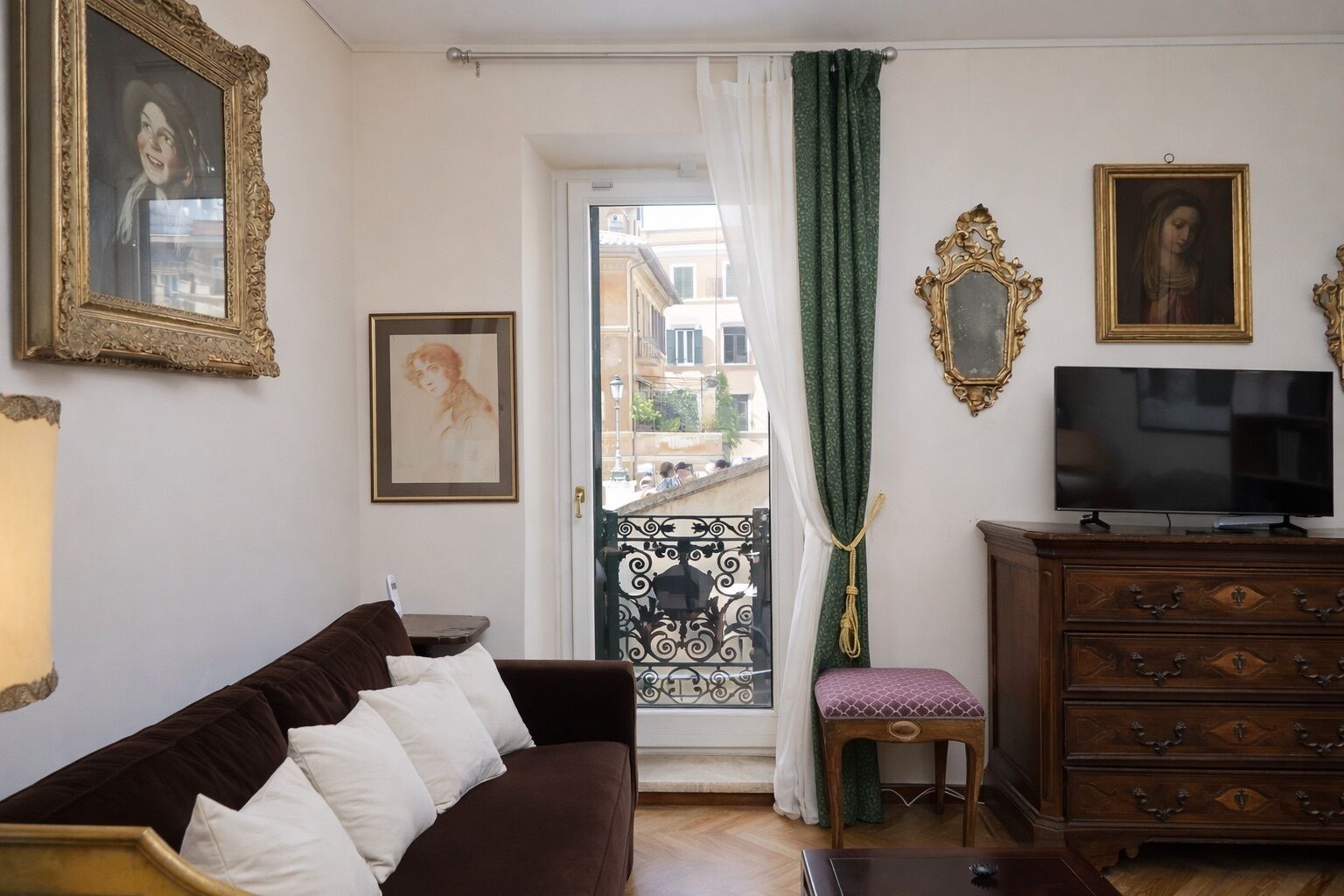 A living room with a brown sofa, a television, a wooden cabinet, and a balcony with a decorative gate.