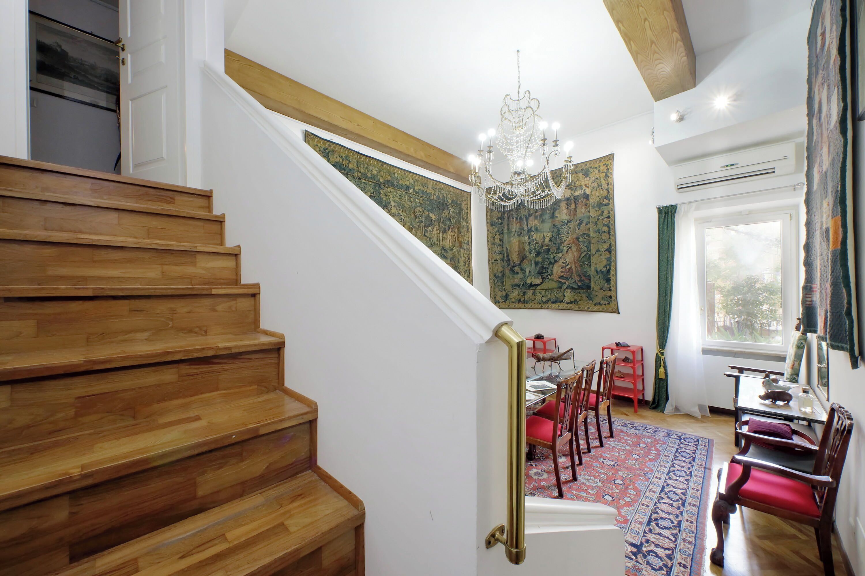 Eine Treppe mit Holzdielen führt zu einem Essbereich mit roten Stühlen und einem gemusterten Teppich.