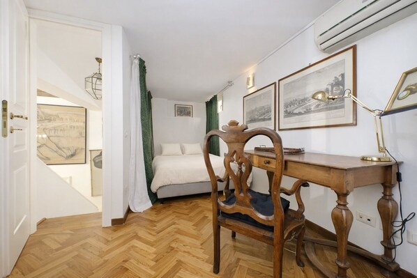 A bedroom with a wooden desk, a chair, a bed, and framed pictures on the wall. - On The Steps (Rome)