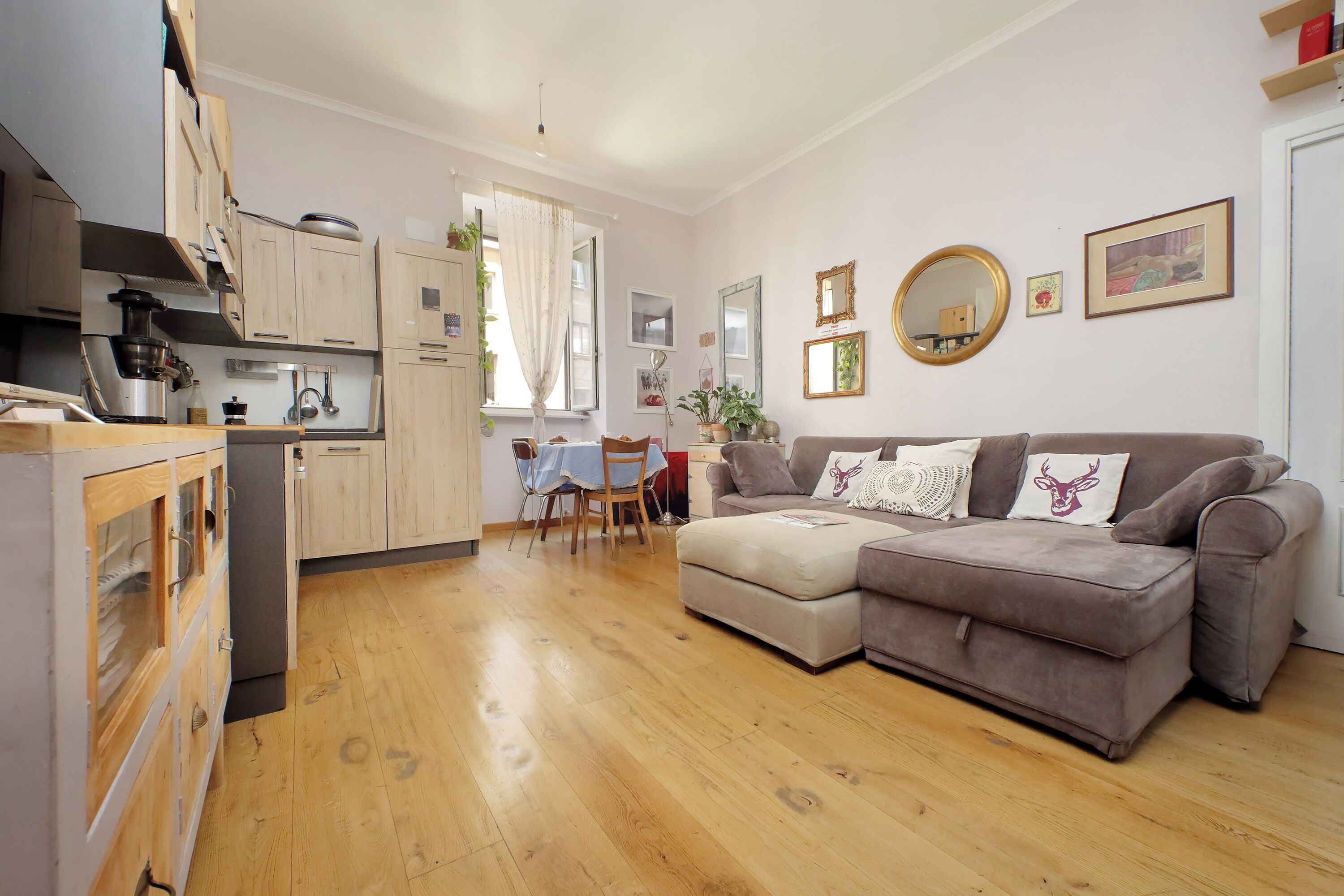 A modern kitchen with wooden cabinets, a dining table with chairs, and a grey sofa in the living area.