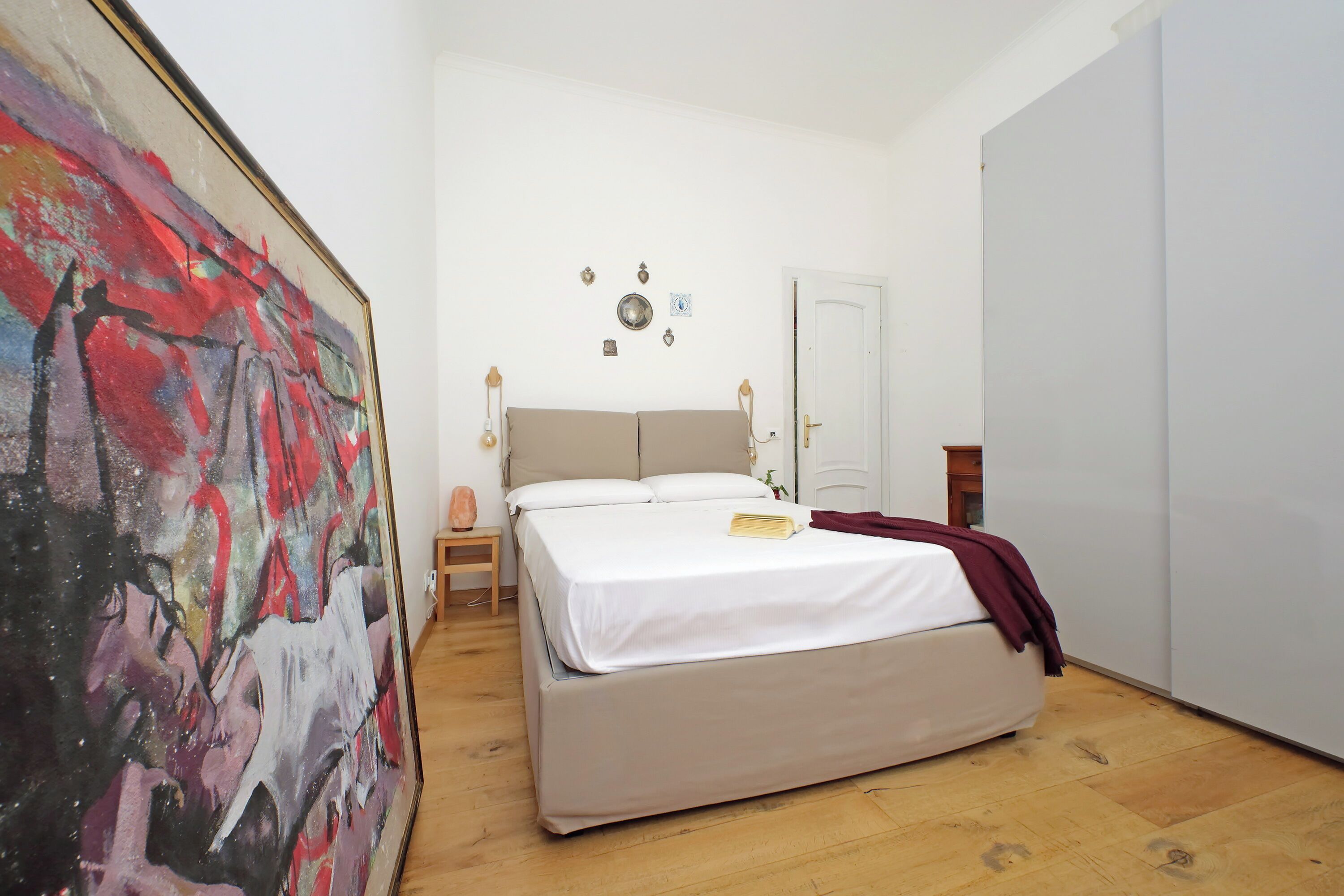 Une chambre à coucher avec un lit, une table de chevet, une lampe et un tableau accroché au mur.
