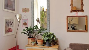 Huoneessa on suuri peili, lattiavalaisin ja useita ruukkukasveja, jotka on sijoitettu puiseen lipastoon.