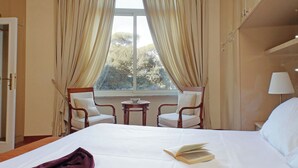 A hotel room with a bed, two chairs, a small table, and a window with curtains. - Borghese Park View (Rome)
