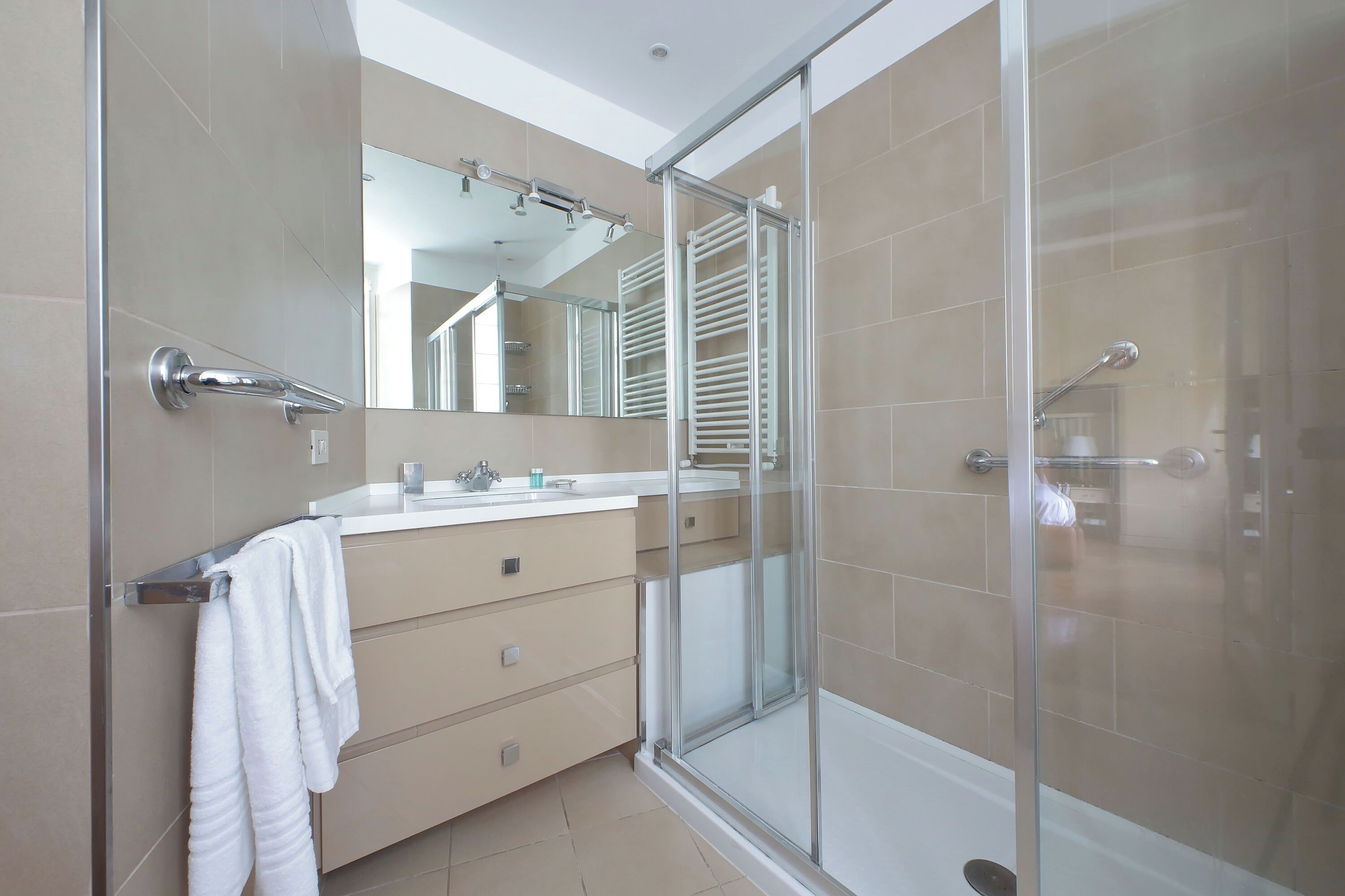 A modern bathroom with a glass shower enclosure, a vanity with a mirror, and beige tiles.