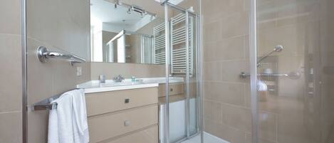 A modern bathroom with a glass shower enclosure, a vanity with a mirror, and beige tiles.