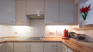 Una cocina moderna con armarios blancos, encimera de madera, cafetera roja y un jarrón con flores rojas en el estante.