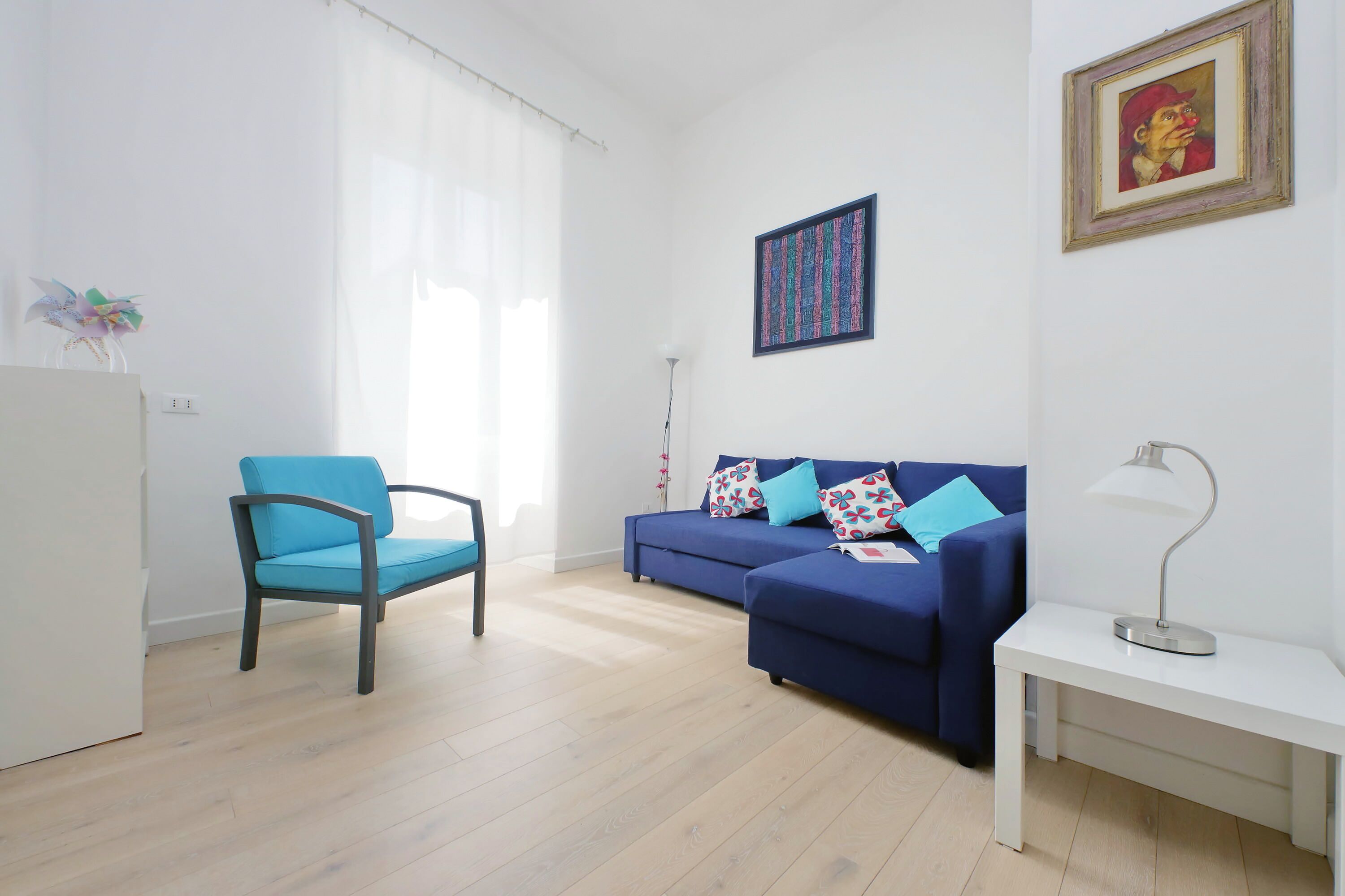 Una sala de estar con un sofá azul, un sillón azul, una mesa blanca y una lámpara de pie.
