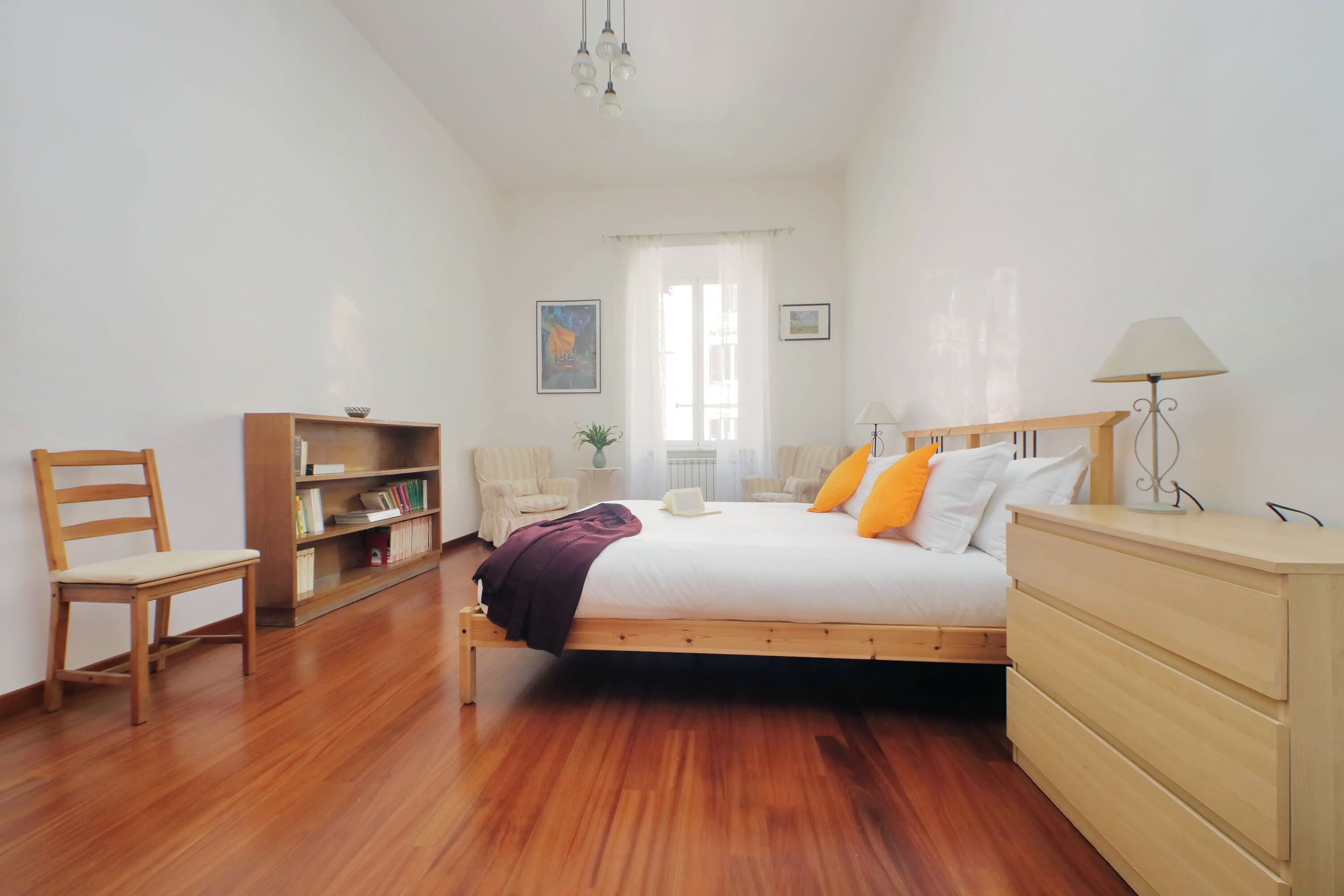 Una camera da letto con un letto in legno, un comodino, una sedia, una libreria e una lampada da terra.