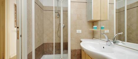 A modern bathroom with a glass-enclosed shower, a white sink with a mirror, and beige tiles.