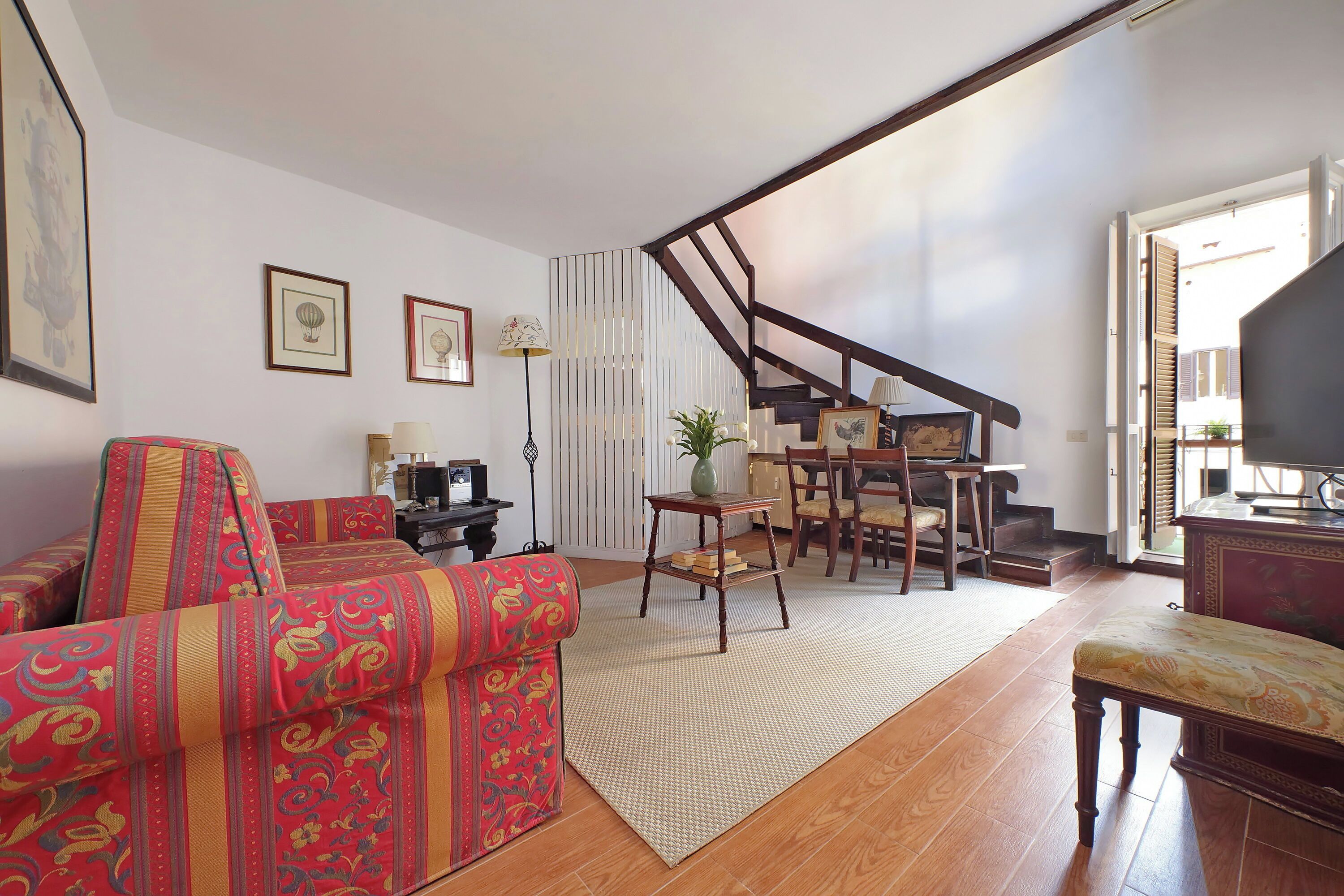 Ein Wohnzimmer mit Sofa, Couchtisch und Fernseher. Eine Treppe führt zu einer weiteren Ebene.