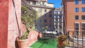 Un balcon agrémenté d’un gazon synthétique vert, de plantes en pot et d’une table dressée pour les repas.