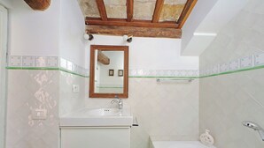 Une salle de bain avec un lavabo blanc, un miroir, une baignoire et des murs recouverts de carreaux verts.