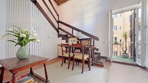 Un escalier avec des rampes en bois menant à l’étage supérieur, un coin repas avec des chaises et une table en bois, et un vase rempli de fleurs blanches posé sur une table d’appoint.
