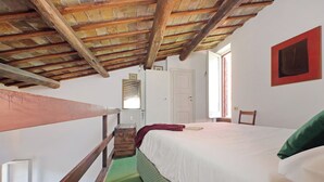 Une pièce avec un plafond en bois, un lit avec une literie blanche, un tapis vert, une chaise en bois et une porte.