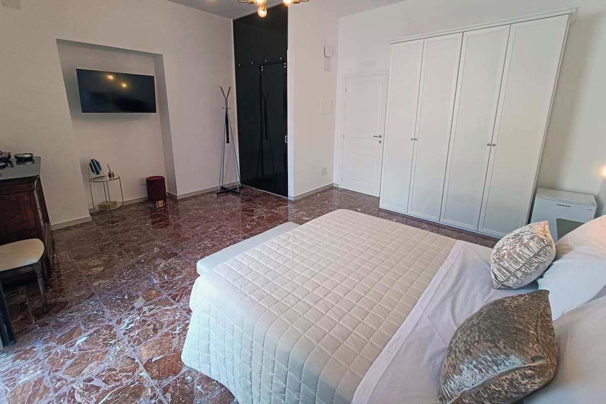Un dormitorio con una cama grande, un televisor montado en la pared, un armario y un escritorio con una silla.