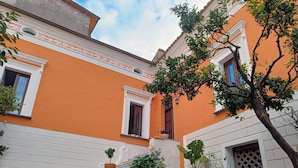 A building with a bright orange facade, white trim, and a set of stone steps leading to a door. - La Residenza del Barone (Camerota)